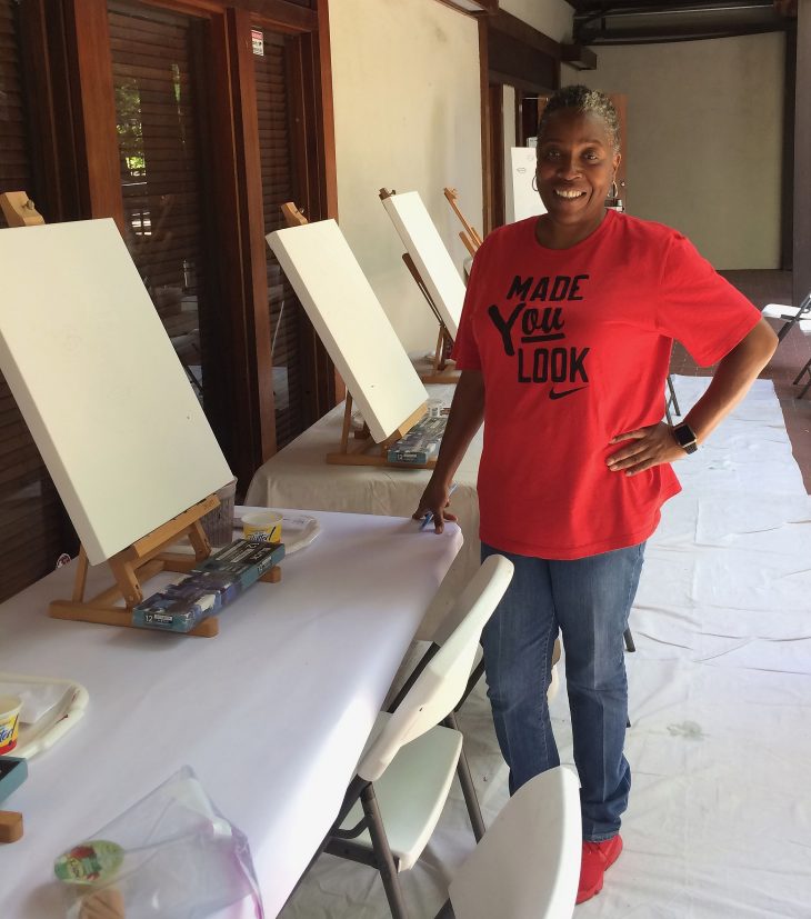 Felisa Gaffney is standing in front of tables with blank canvasses on them.