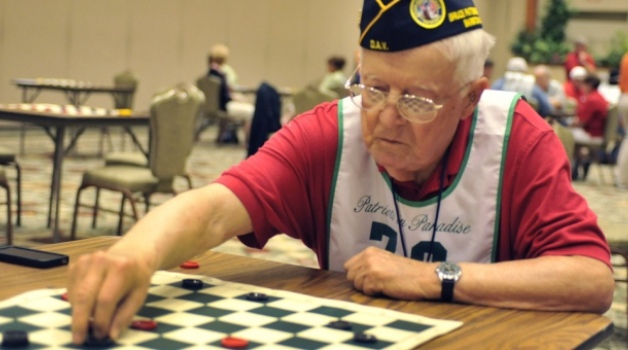 Male Veteran playing checkers at a wooden table.