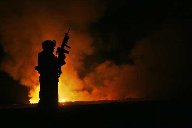 night image of a soldier silhouetted against a burnpit