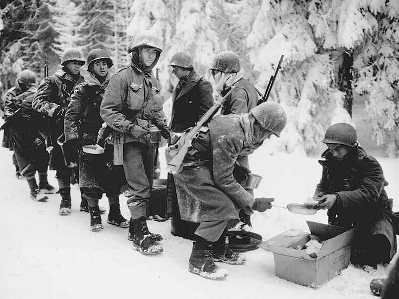 Soldiers with the U.S. Army’s 347th Infantry Regiment line wait for a meal on their way to La Roche, Belgium, during the Battle of the Bulge in January 1945. — Courtesy of the National Archives photo no. 111-SC-198849