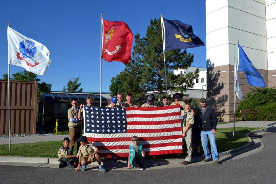 Boy scouts stand around an American Flag in front of a VA Medical Center