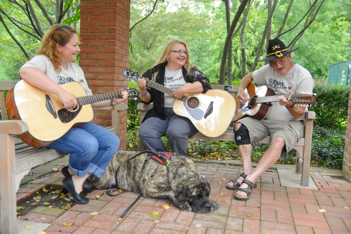 Two women and a man play guitars while a dog sits at their feet.
