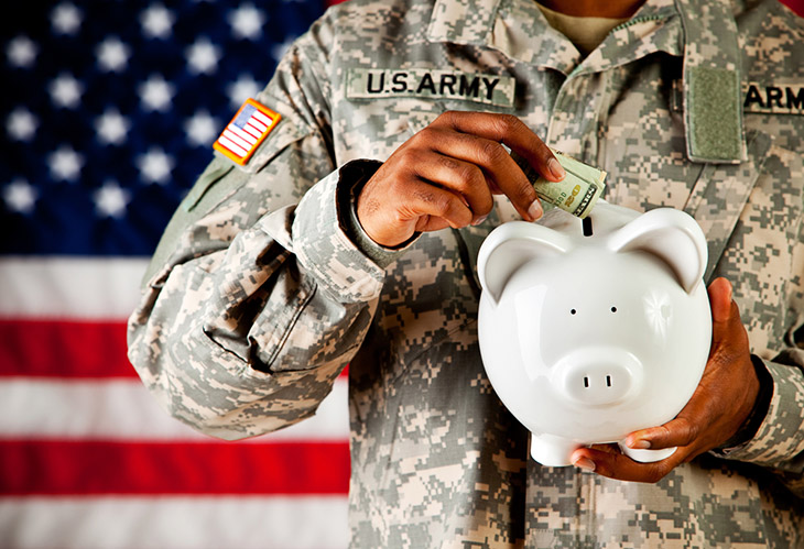 Image of army person in uniform placing money into a piggy bank.