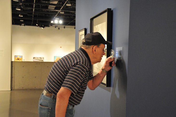 Image of a man using a magnifying glass to read a plaque at a museum.