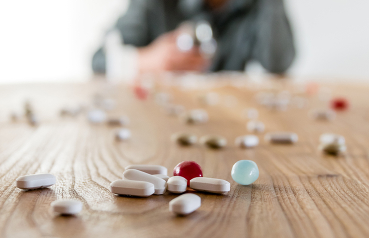 image of pills on a table with a blurred-out person holding a prescription bottle.
