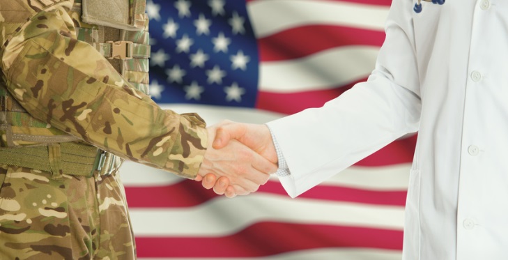 Soldier in uniform and doctor shaking hands with national flag on background - United States