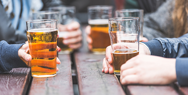 IMage of hands holding beer glasses on a picnic table.
