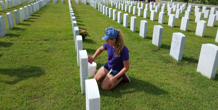 Image: A young girl on her kness cleaning a headstone at Jacksonville National Cemetery