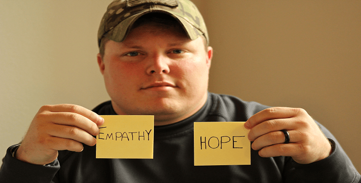 Image of a man holding two post-it notes with the words empathy and hope.