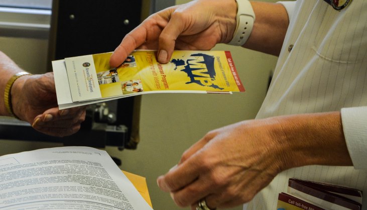 image: Annette Videla, a registered nurse and research coordinator with the Phoenix VA Health Care System’s Million Veteran Program, provides a volunteer a pamphlet explaining the MVP. The Phoenix VA recently surpassed its goal of recruiting 20,000 volunteers into the MVP.