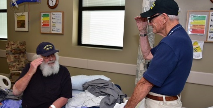 Image: A volunteer salutes a hospitalized Vetern siting on his bed.