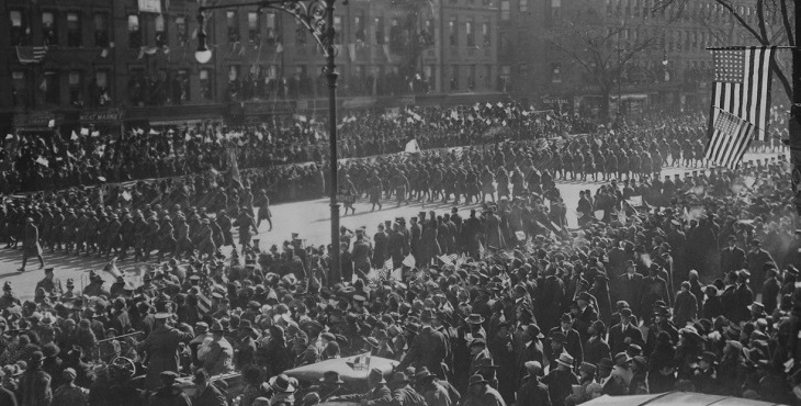 Black and white photograph of the 369th "Harlem Hellfighters" Regiment homecoming parade. Thousands of people line the streets as the soldiers march in formation.