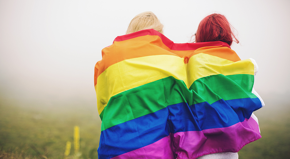 Blonde and redhead woman wrapped in rainbow flag
