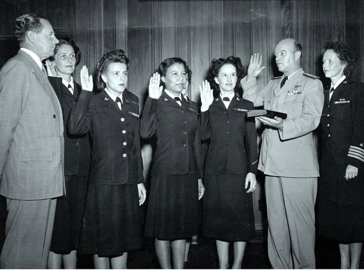 Rear Admiral George L. Russell, USN, (Judge Advocate General of the Navy) Swears in the first six women in the Regular Navy while the Secretary of the Navy John L. Sullivan, far left, looks on. Captain Joy B. Hancock, Director of the Womans Reserve, is next to RADM Russell, July 7, 1948. The first six enlisted women are: Front row: (left to right) Chief Yeoman Wilma J. Marchal, USN; Yeoman Second Class Edna E. Young, USN; Hospital Corpsman First Class Ruth Flora, USN. Second row: (left to right) Aviation Storekeeper First Class Kay L. Langen, USN; (hidden behind the front row): Storekeeper Second Class Frances T. Devaney, USN; and Teleman Doris R. Robertson, USN. Photo courtesy of NHHC.