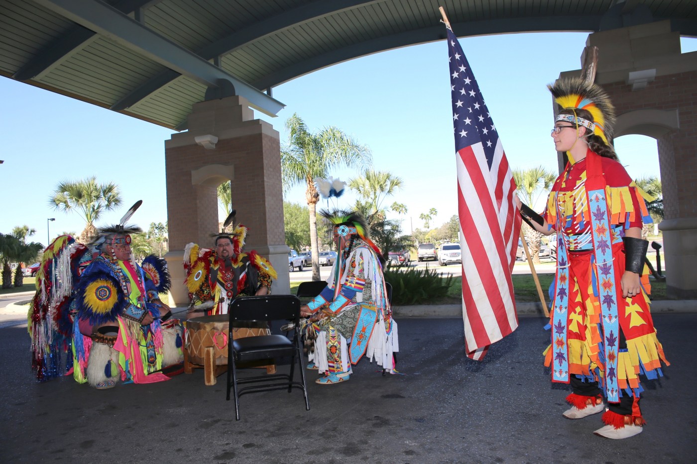 A young male member of the Lipan Apache Tribe of Texas raises the U.S. flag while other tribe members play and sing in a drum circle during a special event held in observance of National Native American Heritage Month, which took place at the VA outpatient clinic in Harlingen, Texas, on November 16, 2018. (U.S. Department of Veterans Affairs photo by Luis H. Loza Gutierrez)