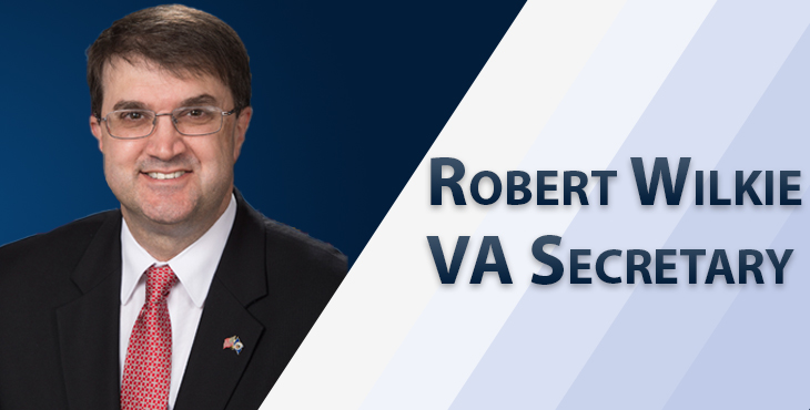 Picture shows the Secretary of the VA with a dark blue background and diagonal stripes. Text reads: Robert Wilkie - VA Secretary