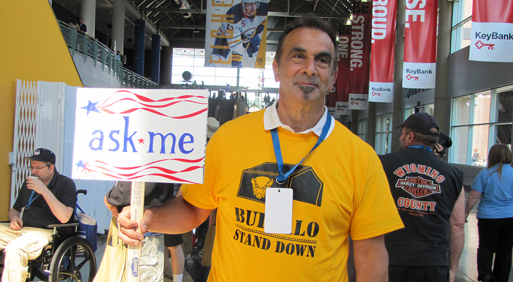 Man holding a ASK ME sign at a Stand Down