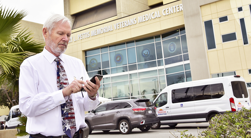 A man checking his mobile phone in front of a VA Medical Center