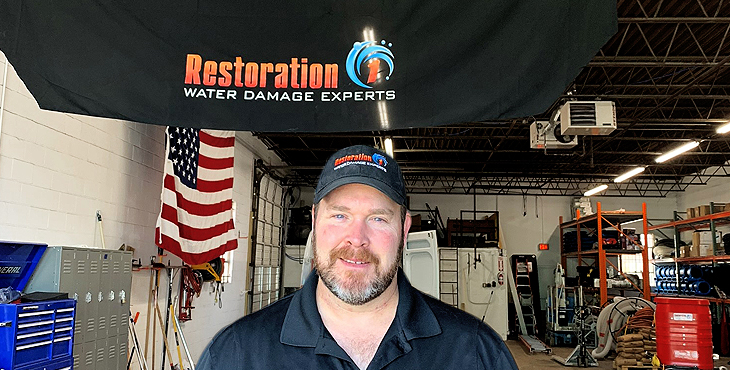 Graphic for Restoration 1 - shows man looking at camera in a garage with a banner for Restoration 1 hanging overhead.