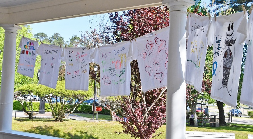 A row of tee shirts bearing slogans that reference military sexual trauma hanging on a clothesline