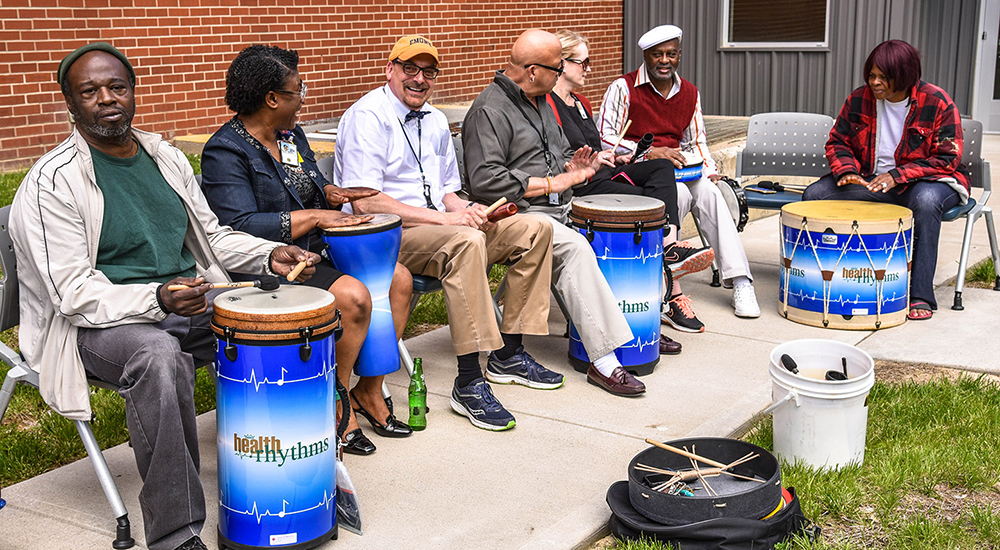 Men and women sitting in chairs with drums outside.