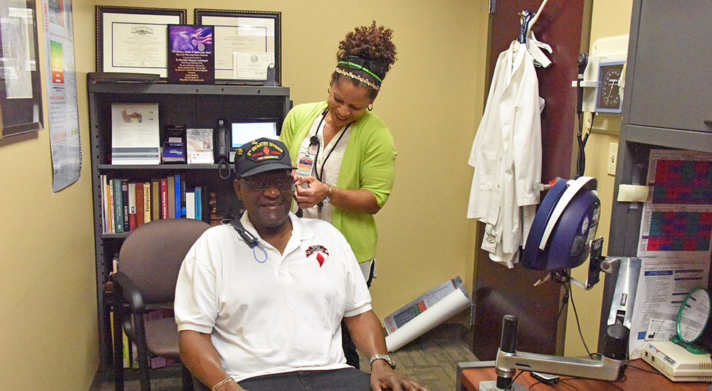 Clinician fits a male Veteran with a hearing aid fitting collar