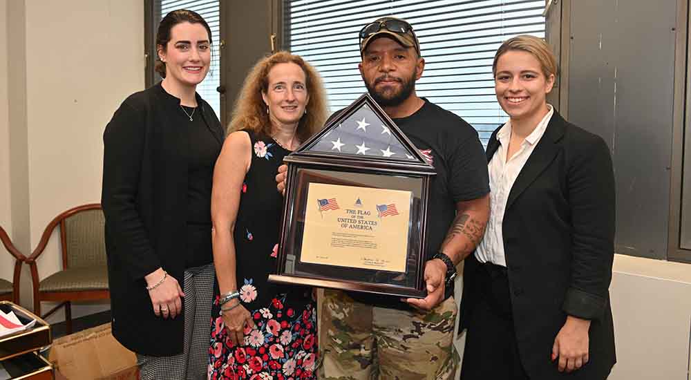 A male Veteran and three female VA clinicians with a flag certificate in a frame.