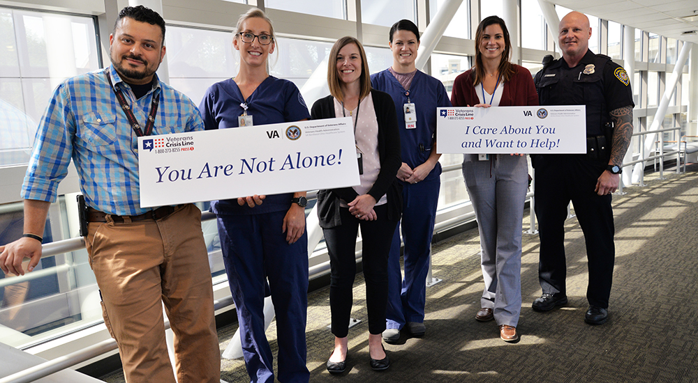 Six men and women standing in a hallway holding suicide prevention message signs.