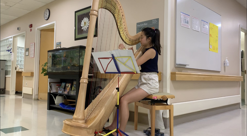 A young female musician volunteer plays a harp in a hospital hallway