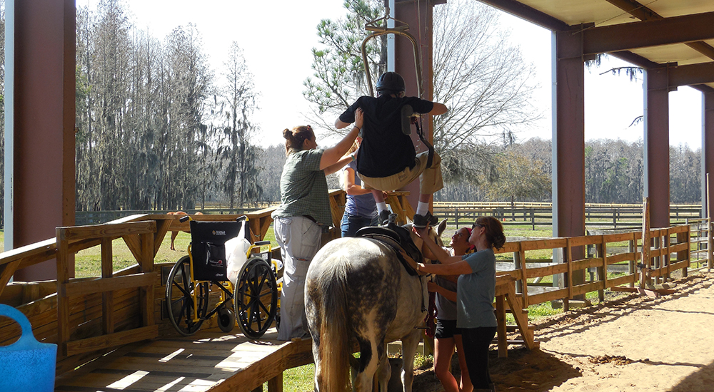 Four people help a Veteran onto a horse's back using adaptive equipment