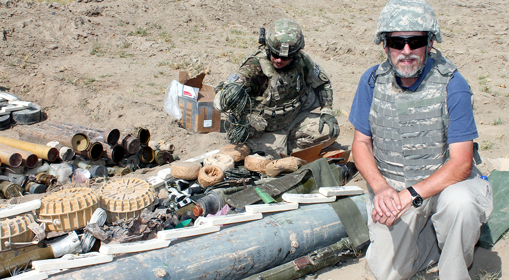 A man kneeling next to munitions in Afghanistan