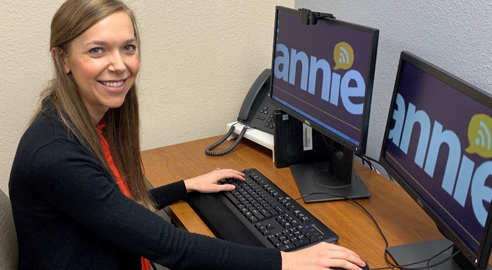 woman at computer with two monitors with the word Annie on each monitor