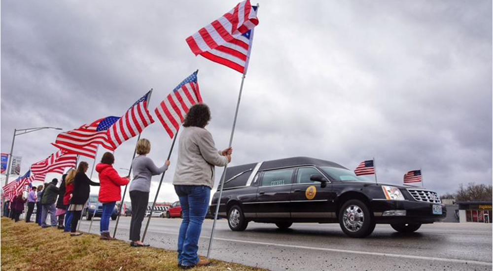 People hold flags as a funeral hearse passes