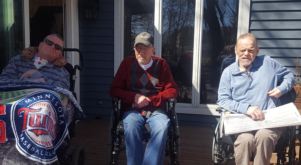 Three men sit outside a medical foster home in wheelchairs