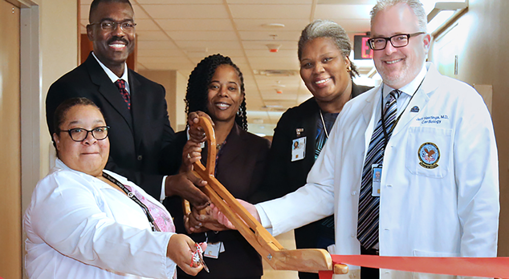 Group of people use large scissors to cut a ribbon opening a hospital wing