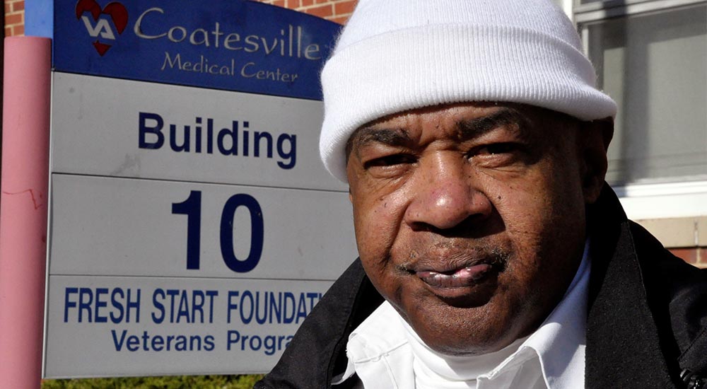 A man in a white watch cap stands in front of the Coatesville VA Medical Center