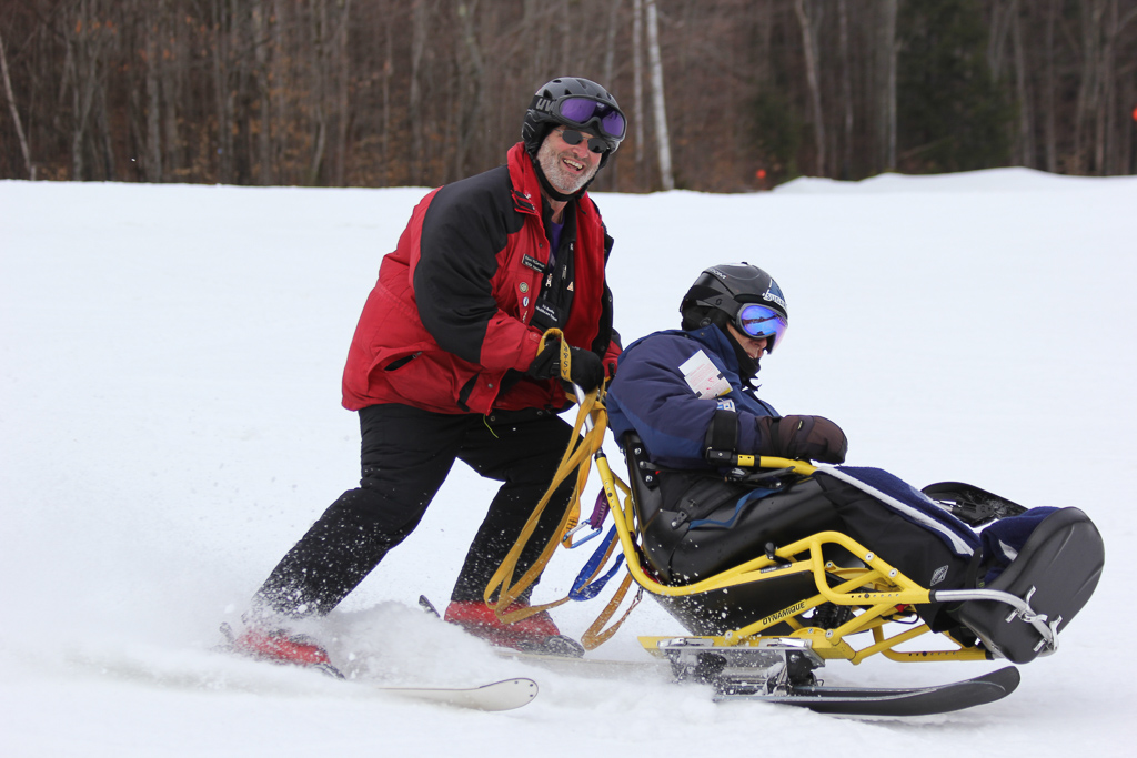 A VA volunteer assists a Veteran with skiing at the New England Winter Sports Clinic for Veterans with Disabilities.