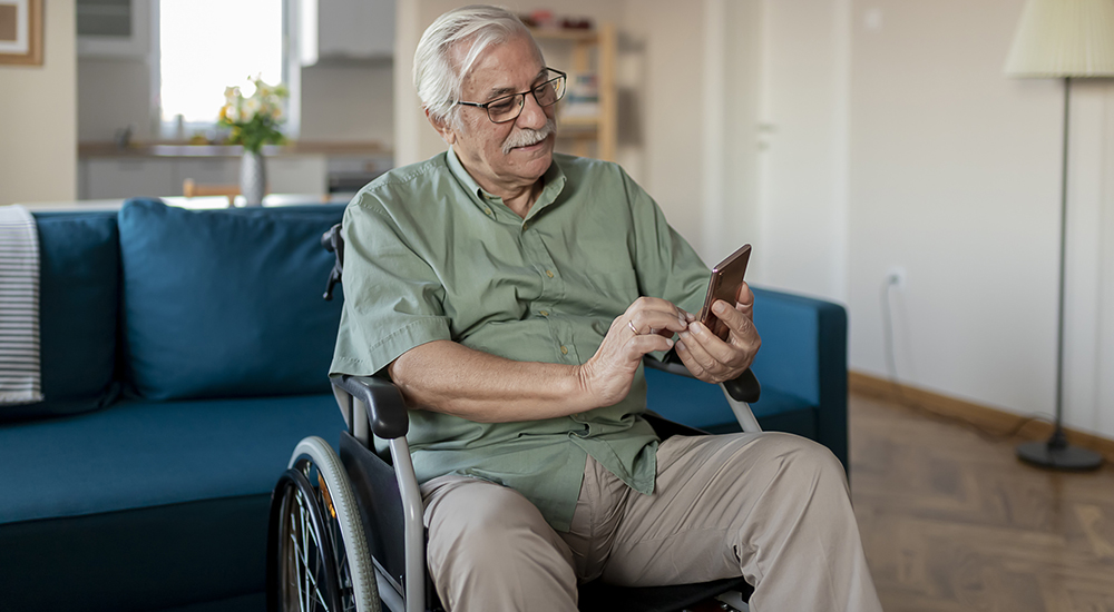 Handicapped senior person sitting in a wheelchair and using a smart phone at home in the living room