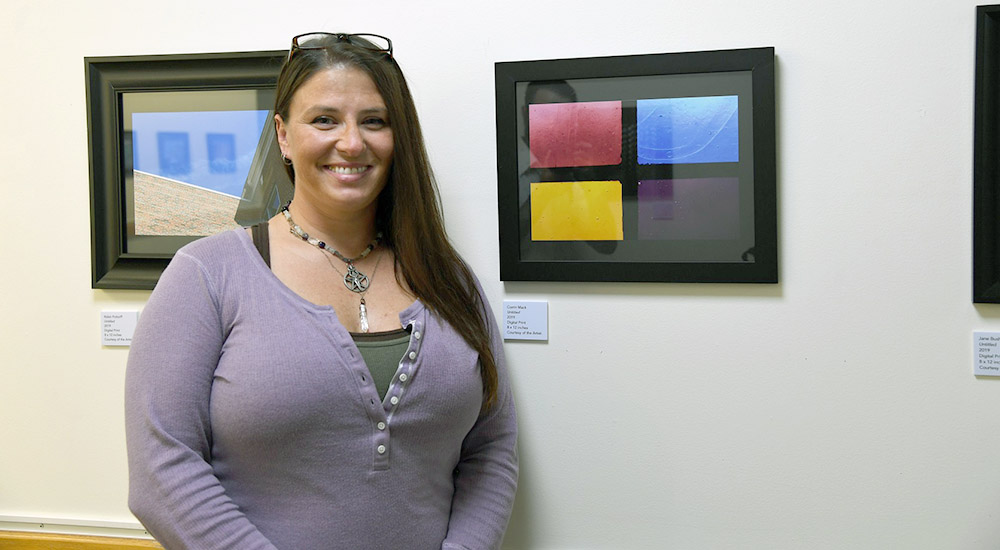 A woman stands in front of her art in a gallery