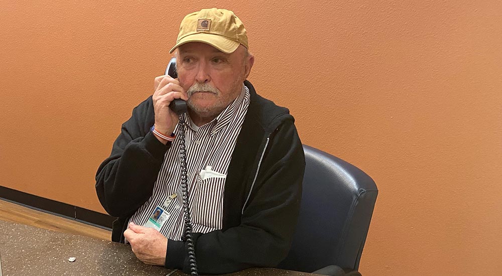 An older man at a desk in a lobby, speaking on the telephone