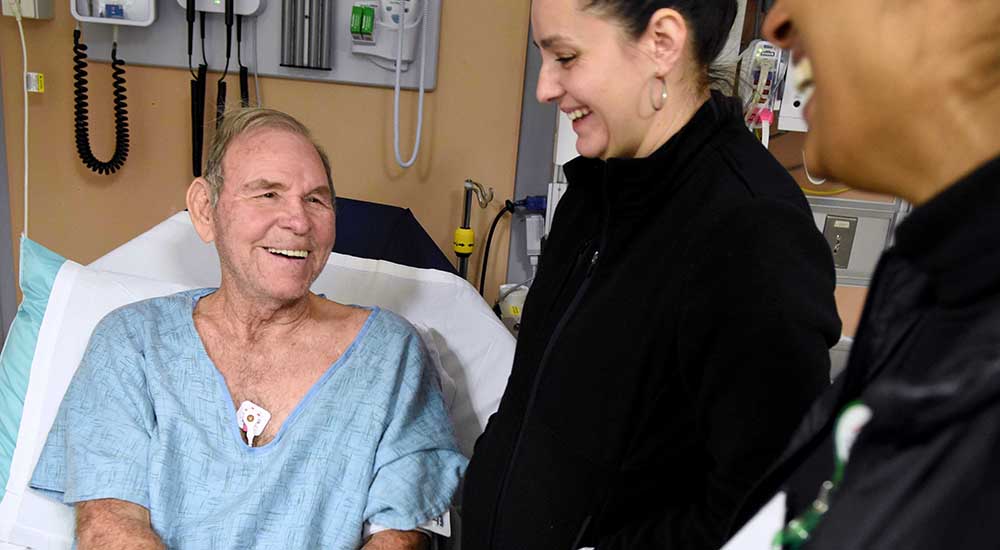 Smiling man in hospital bed talking to a nurse