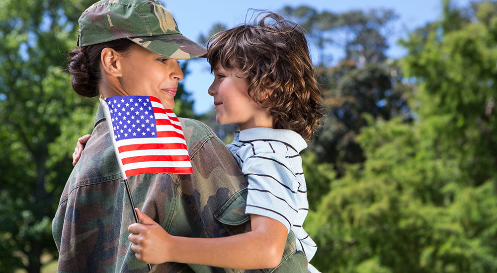Woman soldier in uniform holds a boy who is holding an American flag