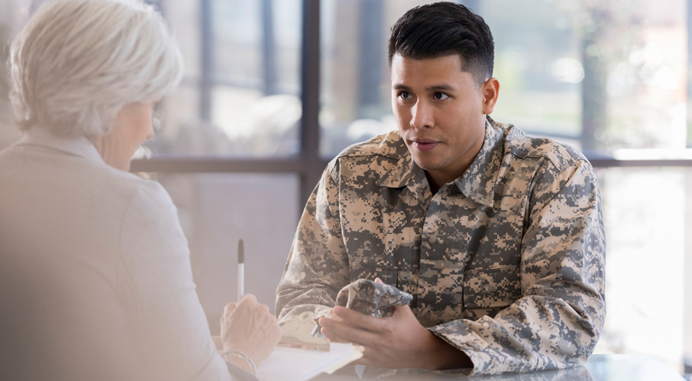 Young army soldier listens as a female therapist gives him advice regarding low blood sugar. The therapist is taking notes in the patient's chart.