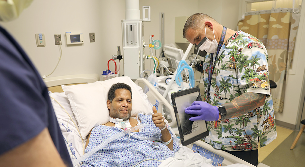 Man in hospital bed enjoys a virtual visit with family on computer tablet