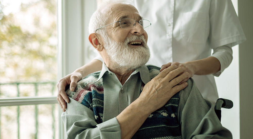 Senior man sitting on the wheelchair, laughing and holding his hospice nurse's hand