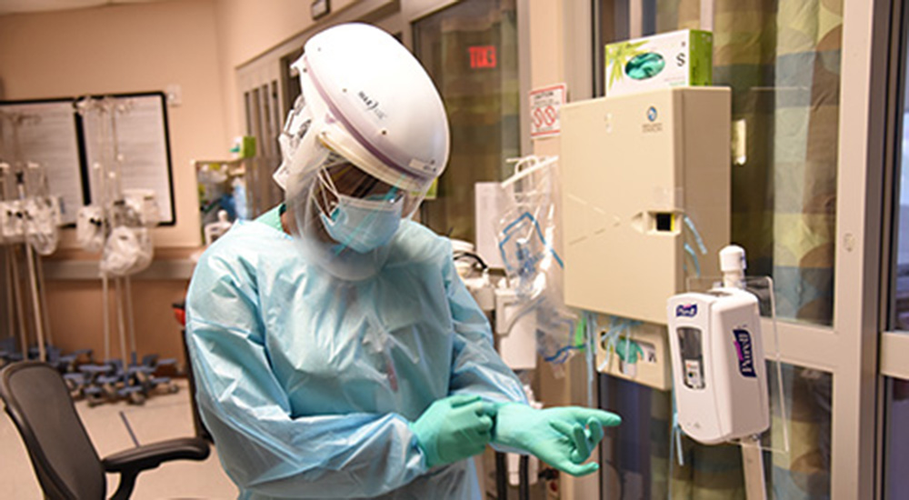 A clinician puts on full PPE protection before providing work on COVID clinical trials
