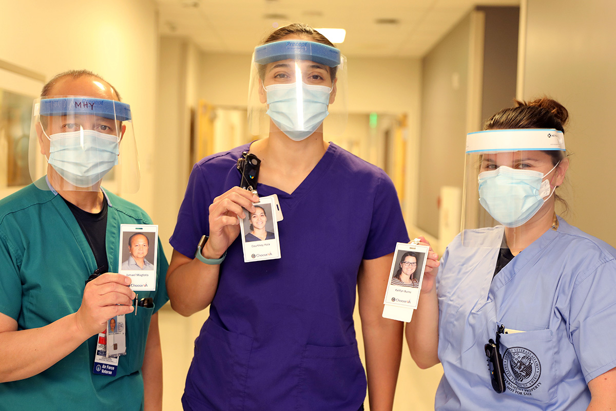 Three nurses, each wearing a mask for safety, hold up photo badges