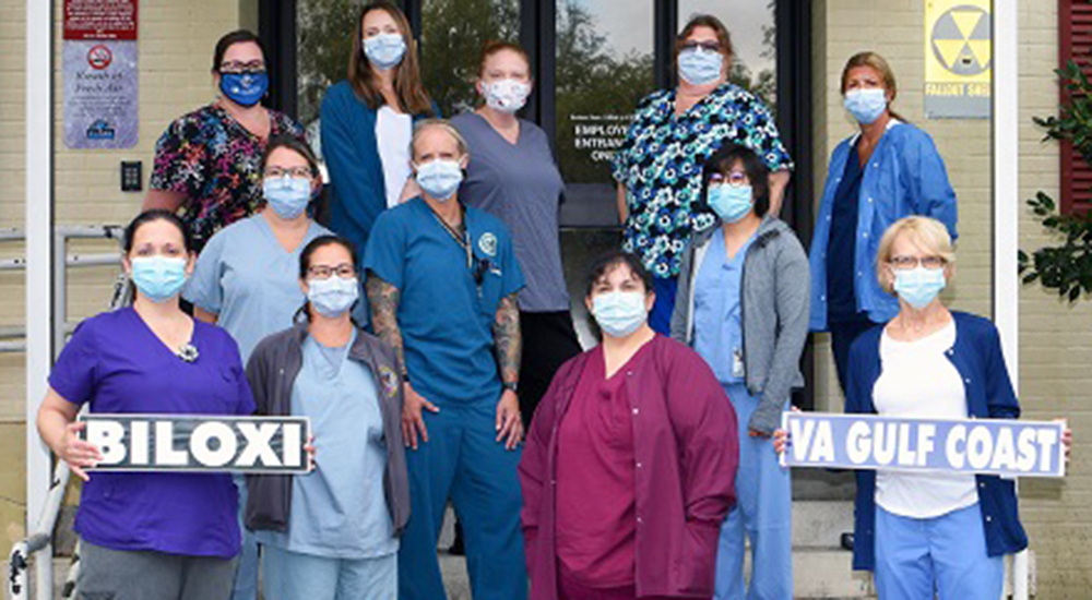 Twelve nurses wearing masks at hospital entrance and holding signs that say Biloxi and VA Gulf Coast