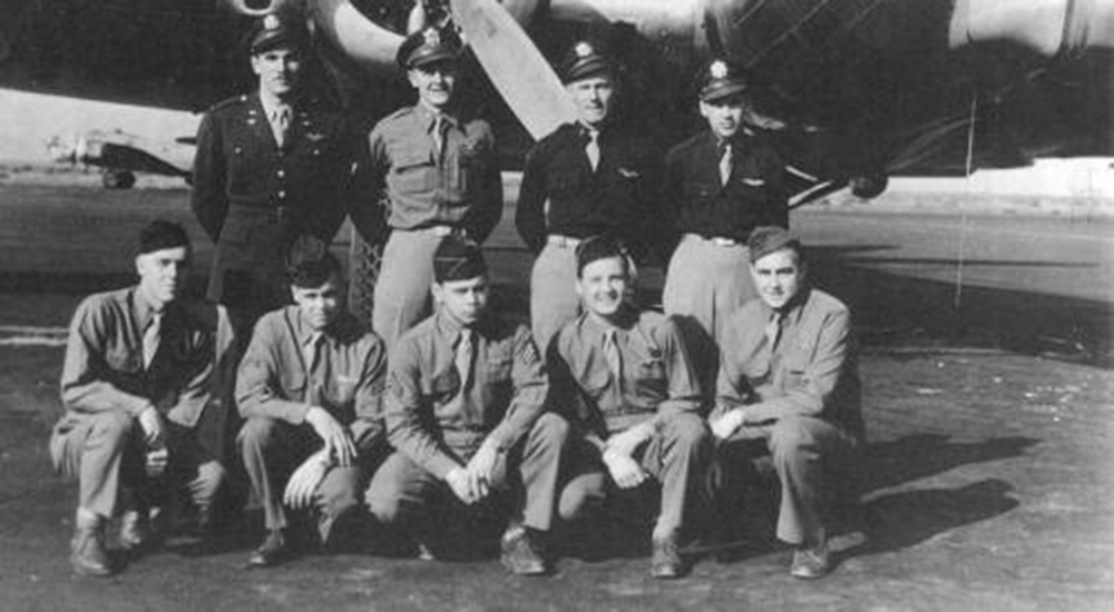 Nine men in uniform in front of airplane