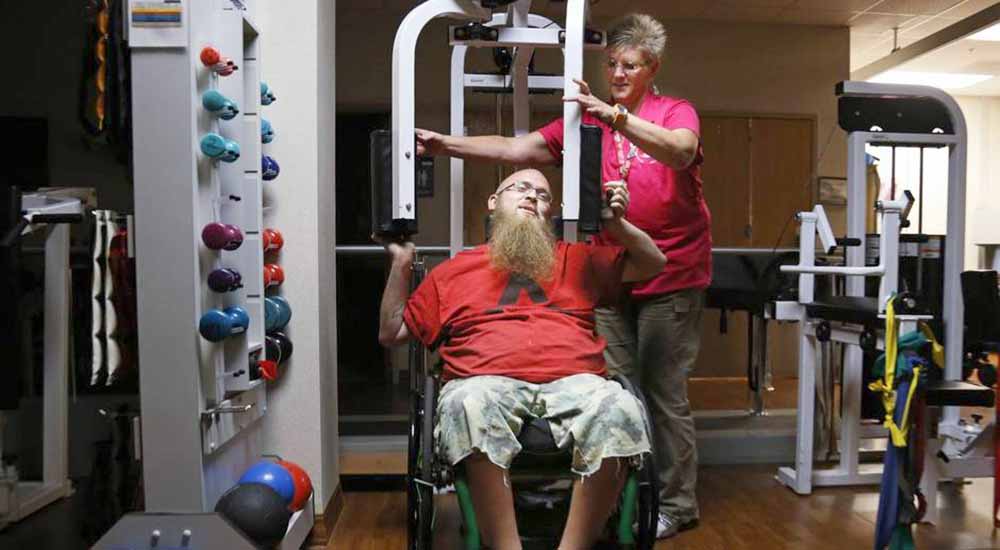Woman assisting man in wheelchair on exercise machine